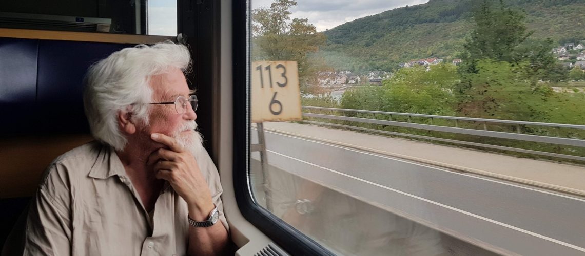nomin-an-elderly-man-looks-out-the-window-of-a-moving-train-on-a-beautiful-landscape-journey_t20_09aBbw